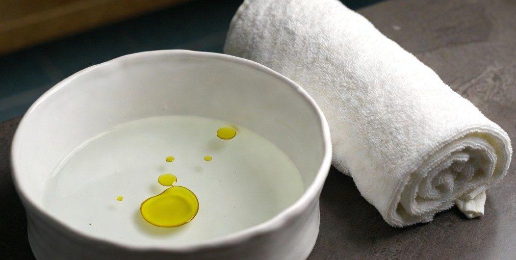 A white bowl of oil beside a rolled towel